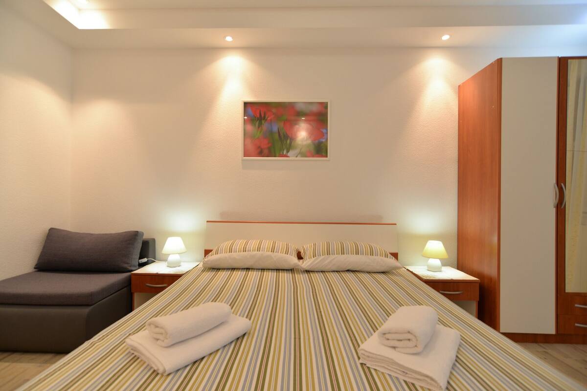 A hotel room with a bed, two bedside lamps, a nightstand, a small sofa, and a painting on the wall.