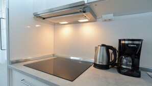 Ett kök med en svart induktionshäll, en silverfärgad vattenkokare och en svart kaffebryggare på bänkskivan.