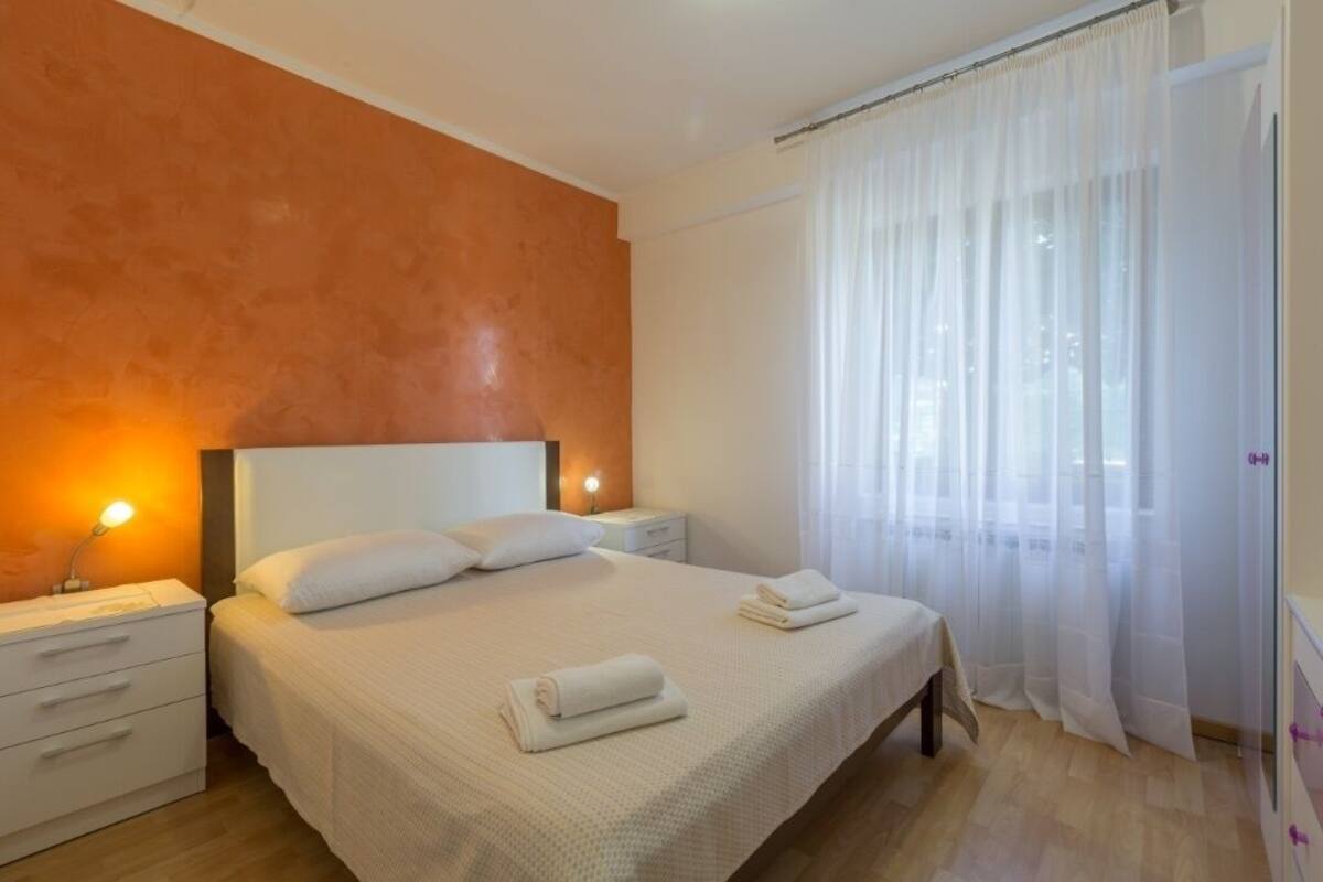 A bedroom with a bed, nightstands, and a window with sheer curtains.