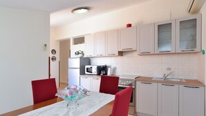 A compact kitchen with white cabinets, a microwave, a coffee maker, and a sink. There is a dining table with a lace tablecloth and a red chair. - Apartment 250 (Fazana)