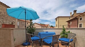 Une terrasse extérieure avec une table et des chaises, un parasol bleu et une vue sur les bâtiments environnants.