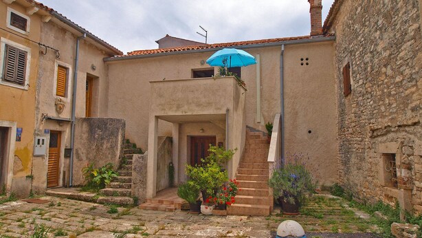 Une cour dallée de pierres, un escalier et un parasol bleu.
