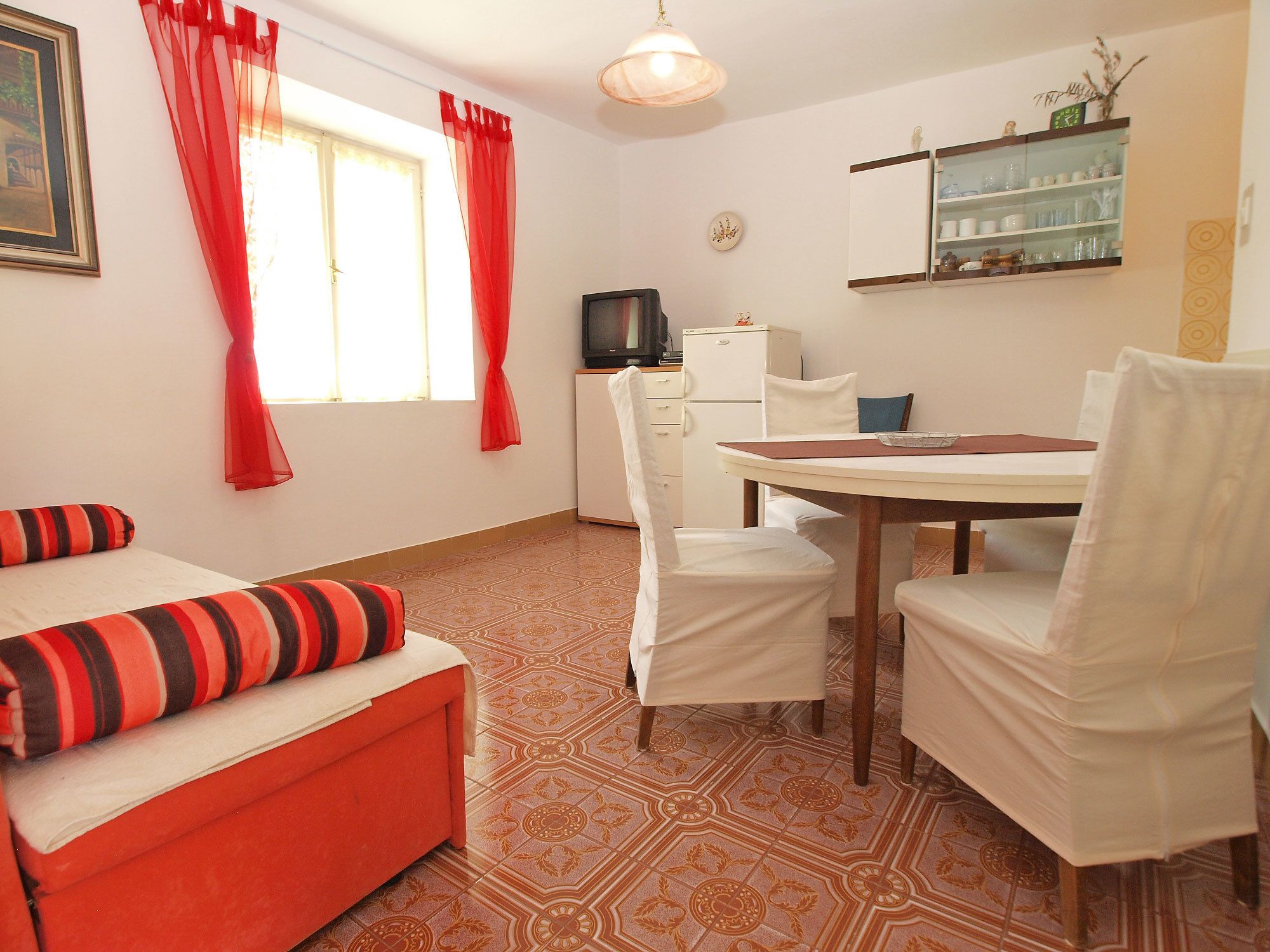 A room with a bed, a dining table with chairs, a television, and a refrigerator.