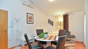 A dining area with a round table, four chairs, a potted plant, and a bed with a patterned bedspread. - Apartment 258 (Pula)