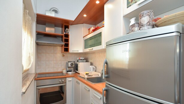A compact kitchen with a built-in oven, a coffee maker, and a stainless steel refrigerator. - Apartment 258 (Pula)