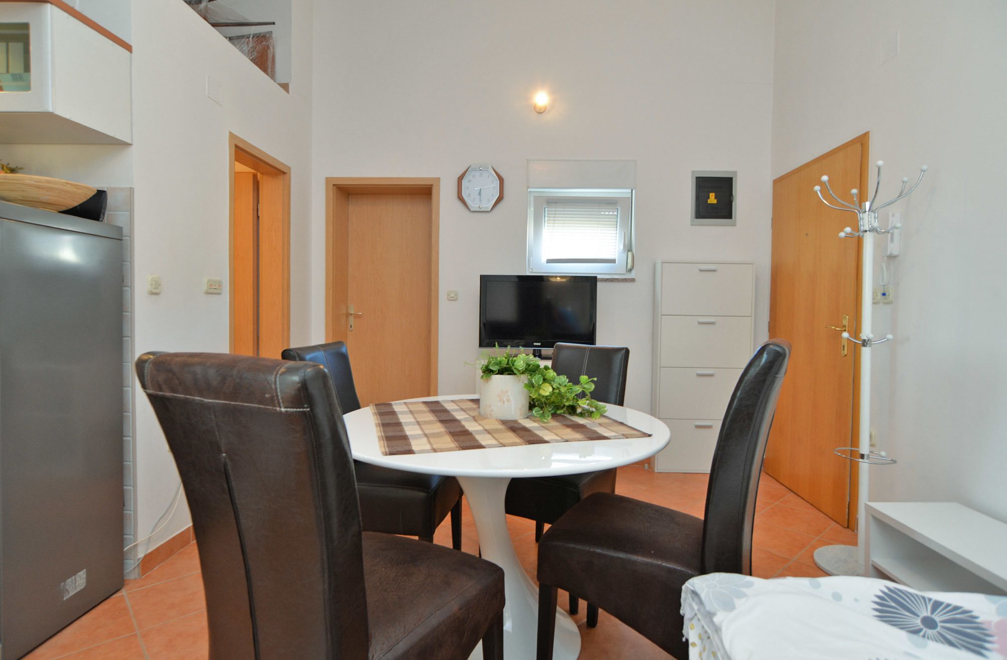 A compact kitchen with a dining area, including a table with chairs, a clock, and a television.