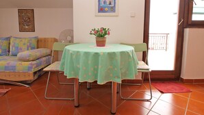 A living room with a sofa, a dining table with a green tablecloth, a potted plant, and a picture on the wall. - Apartment 297 (Porec)
