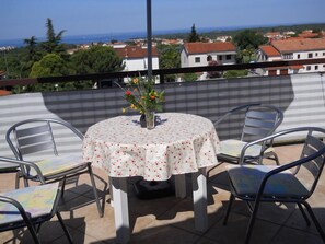 A round table with a floral tablecloth and four metal chairs on a balcony with a view of the sea and buildings. - Apartment 297 (Porec)