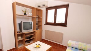 A compact living space with a television on a wooden stand, a small table with a plate, a radiator, and a window with a view. - Apartment 297 (Porec)