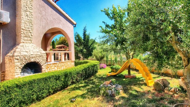 A stone building with a brick oven, a well-maintained garden with hedges, and a yellow slide. - Apartment 316 (Fazana)