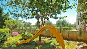 A yellow slide in a garden with a tree and various plants. - Apartment 316 (Fazana)