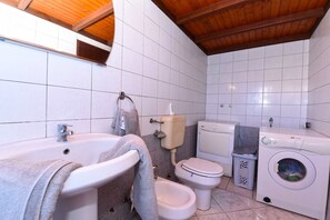 A bathroom with a bathtub, sink, toilet, bidet, and washing machine.