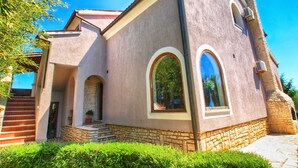 A two-story building with a stone base and a pink stucco exterior. There are two arched windows on the second floor and a small entrance with steps. - Apartment 316 (Fazana)