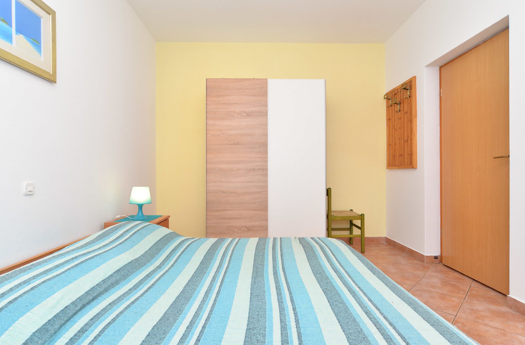 Une chambre à coucher avec un lit, une table de chevet, une lampe, une porte en bois et une chaise.