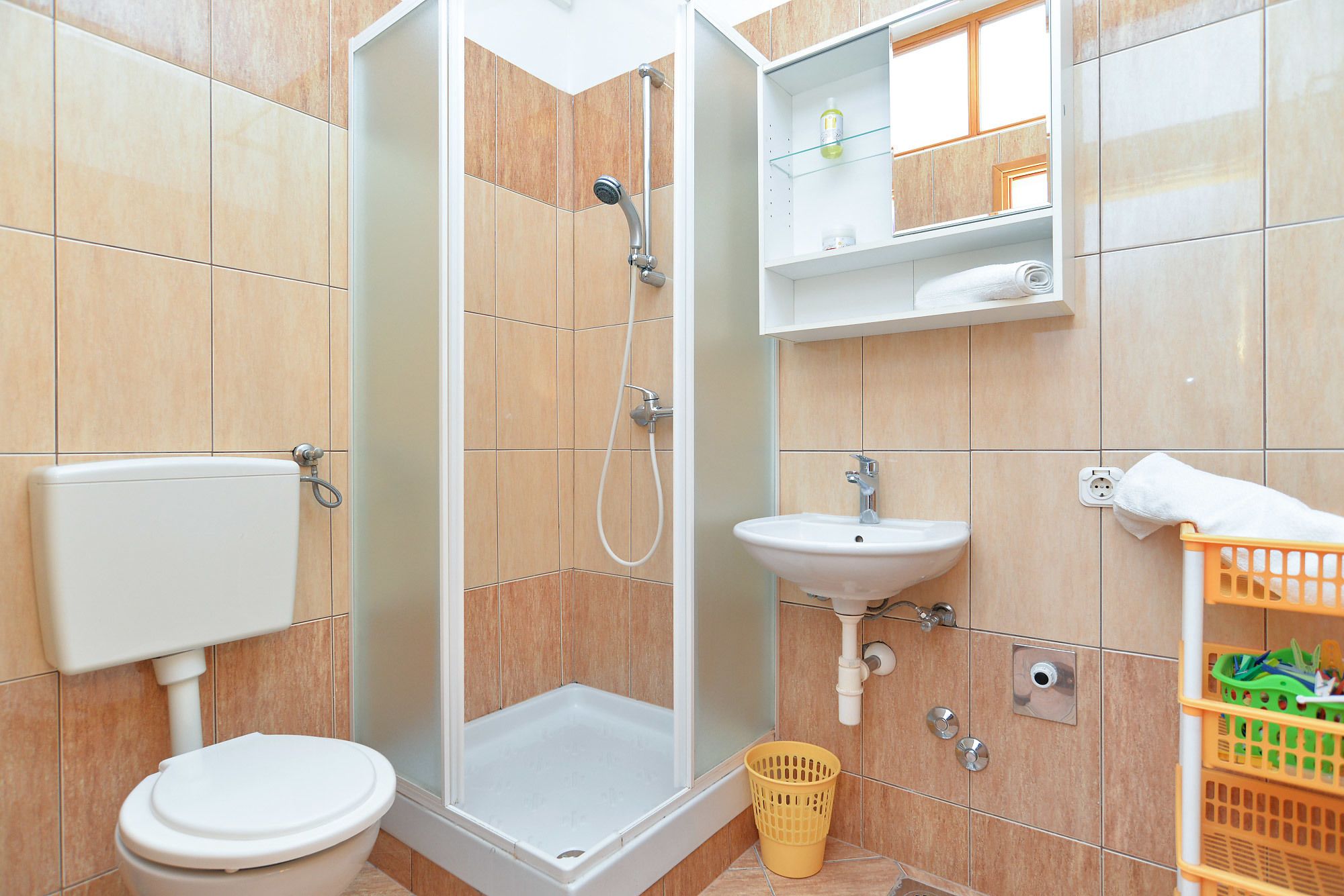 Une salle de bain équipée de toilettes, d’une douche, d’un lavabo et d’une petite étagère où sont rangés les articles de toilette.