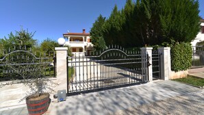 A gated entrance with a metal gate, a potted plant, and a building in the background. - Apartment 344 (Fazana)