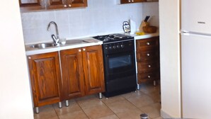 A kitchen with wooden cabinets, a stainless steel sink, a black stove, and a white refrigerator. - Apartment 356 (Umag)