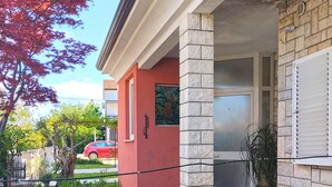 A building with a stone patio, a red door, and a potted plant. - Apartment 356 (Umag)