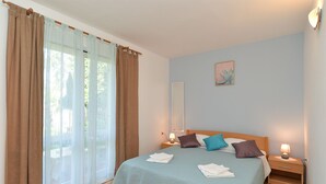 Une chambre à coucher comprenant un lit, deux tables de chevet, une commode, une fenêtre avec des rideaux et une lampe fixée au mur.