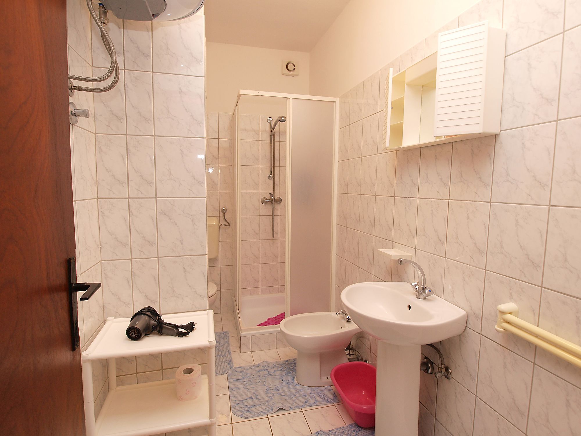 A bathroom with a shower, toilet, bidet, and sink.