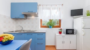 Een keuken met blauwe kastjes, een witte koelkast, een magnetron, een spoelbak en een raam met een plant.