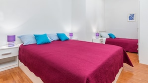 Een slaapkamer met twee bedden, elk voorzien van een rode spreidek en meerdere kussens. Er staan nachtkastjes met lampen en er hangt een kunstwerk aan de muur.