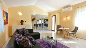 Ein Wohnzimmer mit einer Couch, einem Glastisch und einem violetten Teppich. Es gibt einen Essbereich mit Stühlen und einem Tisch.