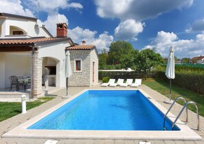 Una piscina con lettini, un edificio in pietra e un giardino.