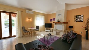 Ein Wohnzimmer mit Sofa, Fernseher, Kamin und einer Essecke mit Stühlen und Tisch.
