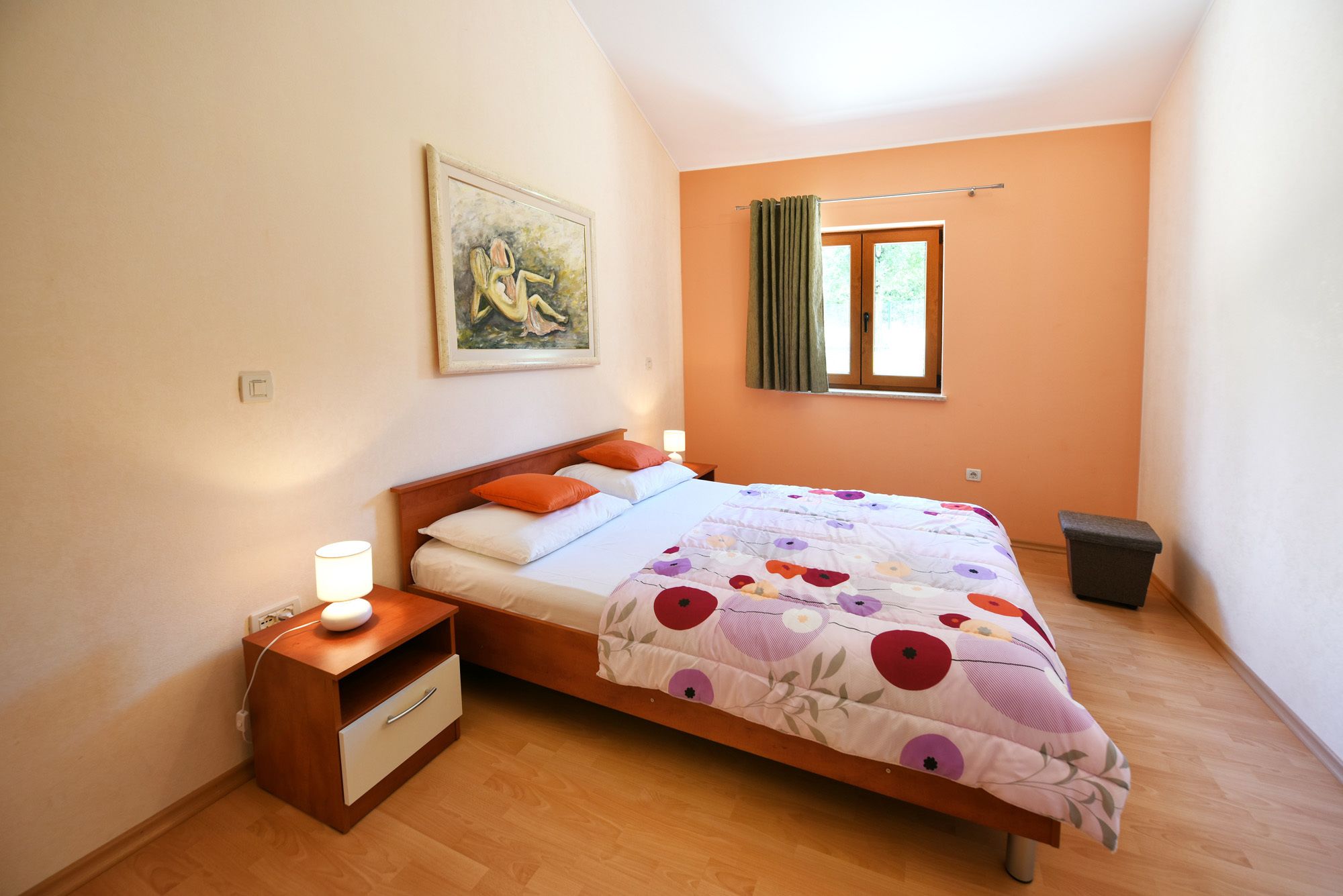 Un dormitorio con cama, mesita de noche, lámpara y un cuadro en la pared.