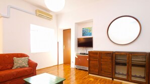 Ein Wohnzimmer mit Holzboden, einem roten Sofa, einem grünen Tisch, einem Fernseher und einem Schrank.