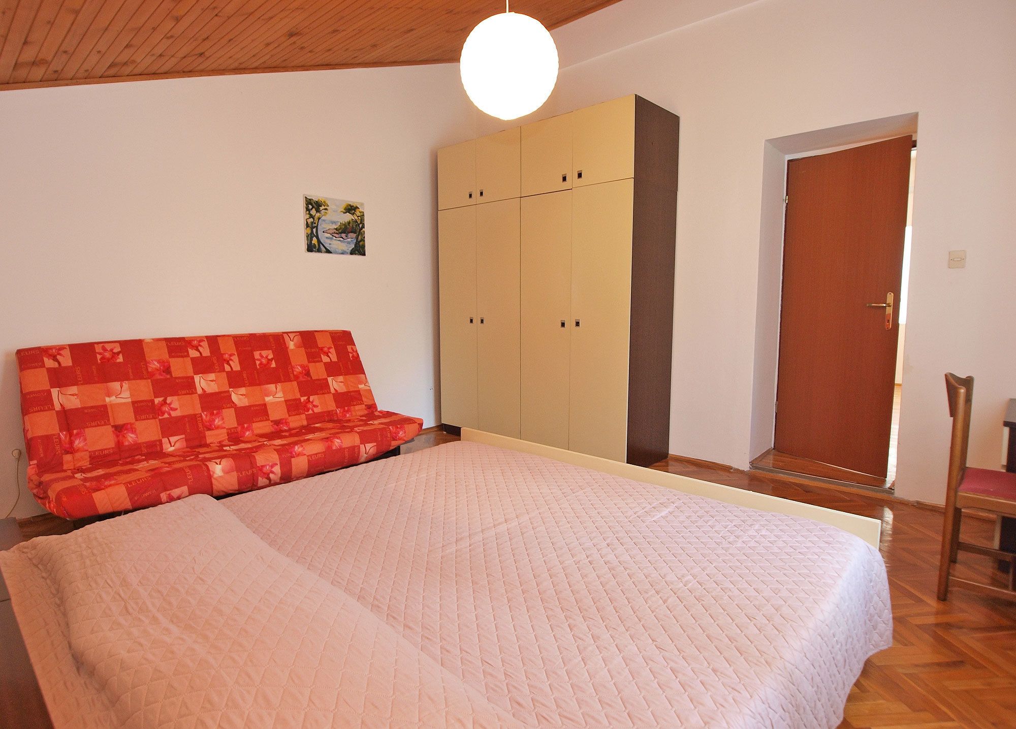 A bedroom with a bed, a sofa, a wardrobe, and a door.