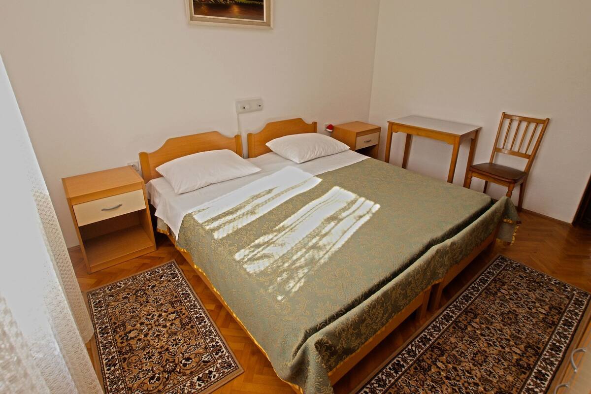A bedroom with a bed, a nightstand, a chair, a small table, and a painting on the wall.