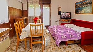 Ein Zimmer mit einem Bett, einem Fernseher, einem Esstisch mit Stühlen, einem roten Sofa und einem Gemälde an der Wand.