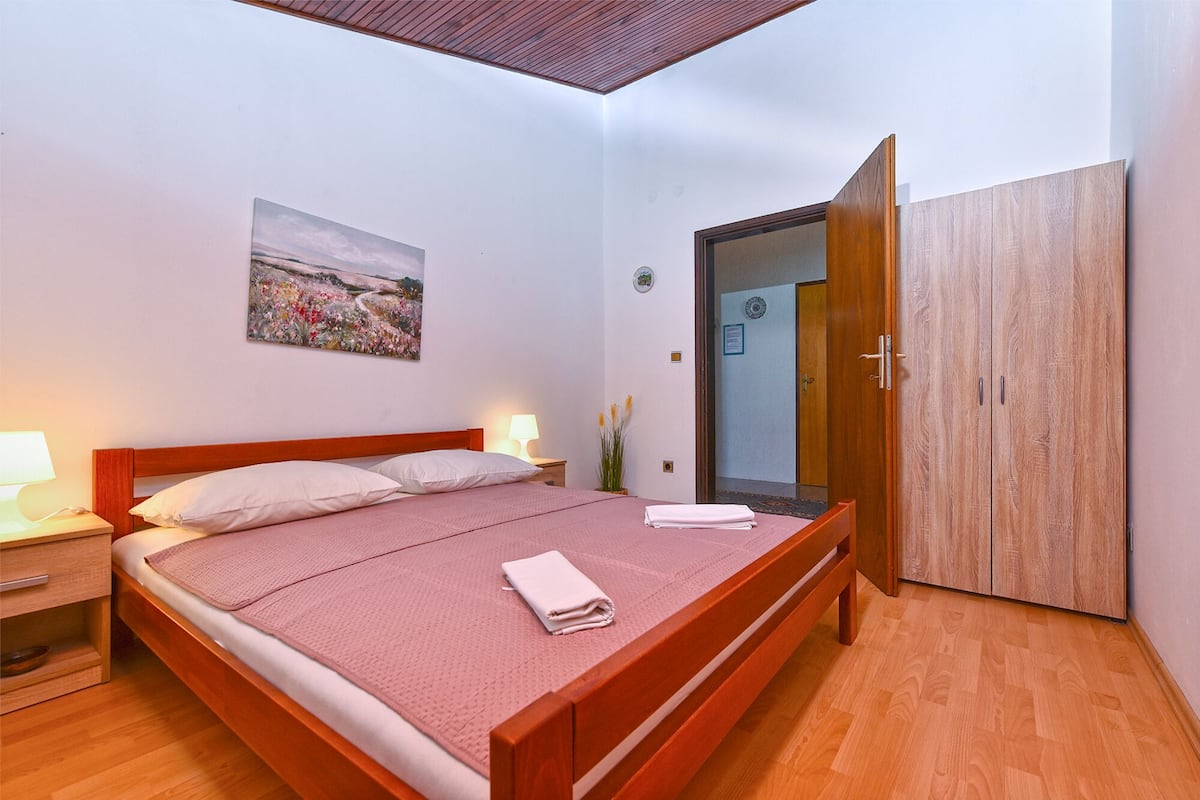 A bedroom with a wooden bed, bedside lamps, a painting, a wardrobe, and a mirror.