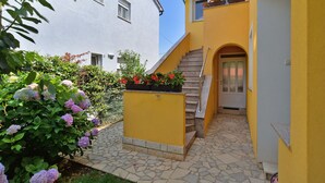 A yellow building with a stone staircase leading to a door, surrounded by greenery and flowers. - Apartment 436 (Fazana)