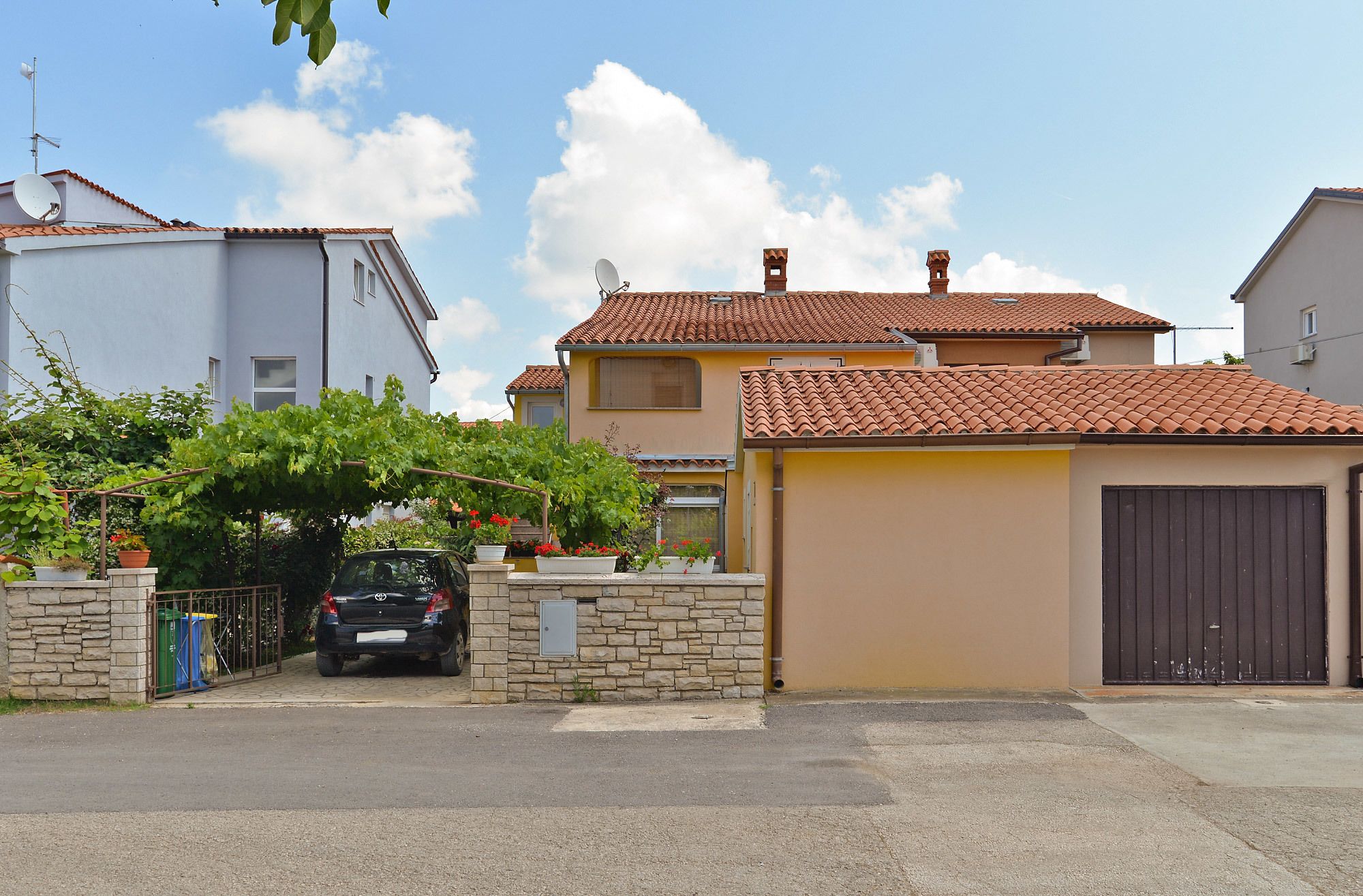 A residential area with houses, a parked car, and a stone wall.