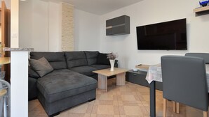 A modern living room with a grey sofa, a coffee table, a TV mounted on the wall, and a small table with a vase. - Apartment 436 (Fazana)