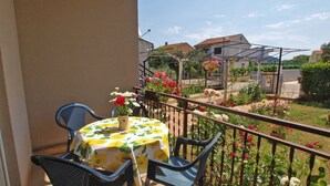 A balcony with a table and chairs, a garden with flowers, and a house in the background. - Apartment 439 (Fazana)