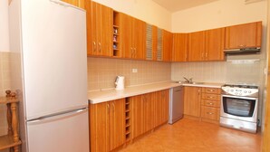 A compact kitchen with wooden cabinets, a white refrigerator, a dishwasher, and a stove. - Apartment 439 (Fazana)
