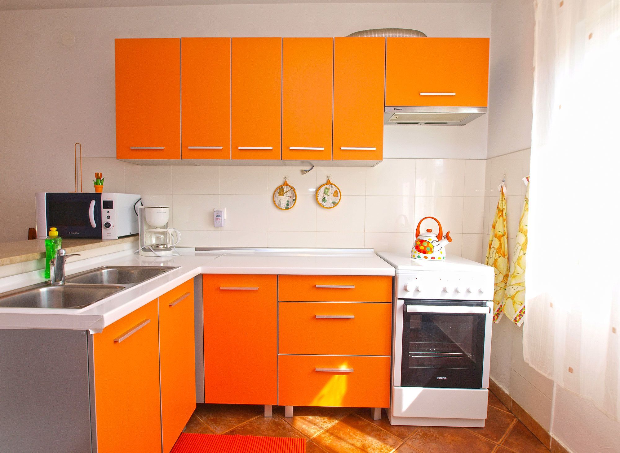 Une cuisine avec des meubles de couleur orange, un four à micro-ondes, une machine à café et un four traditionnel.