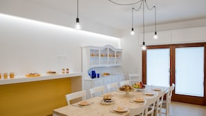 A dining area with a wooden table, white chairs, and a white cabinet with shelves. - B&B Oikos Selinunte (Castelvetrano)
