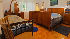 Ein Schlafzimmer mit einem Holzbett, einem Sessel, einem Schminktisch, einem Spiegel, einem Fenster mit Vorhängen und einem Bild an der Wand.