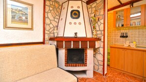 A cozy living room with a fireplace, a stone wall, and a kitchen area with wooden cabinets. - Apartment 498 (Medulin)