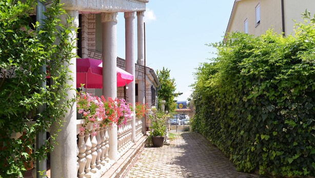 A cobblestone pathway flanked by lush greenery and a building with columns and pink umbrellas. - Apartment 498 (Medulin)