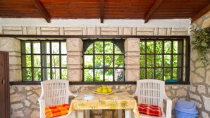 A covered patio with a stone wall, two white plastic chairs, a table with a yellow tablecloth, and a blue trash bin. - Apartment 498 (Medulin)