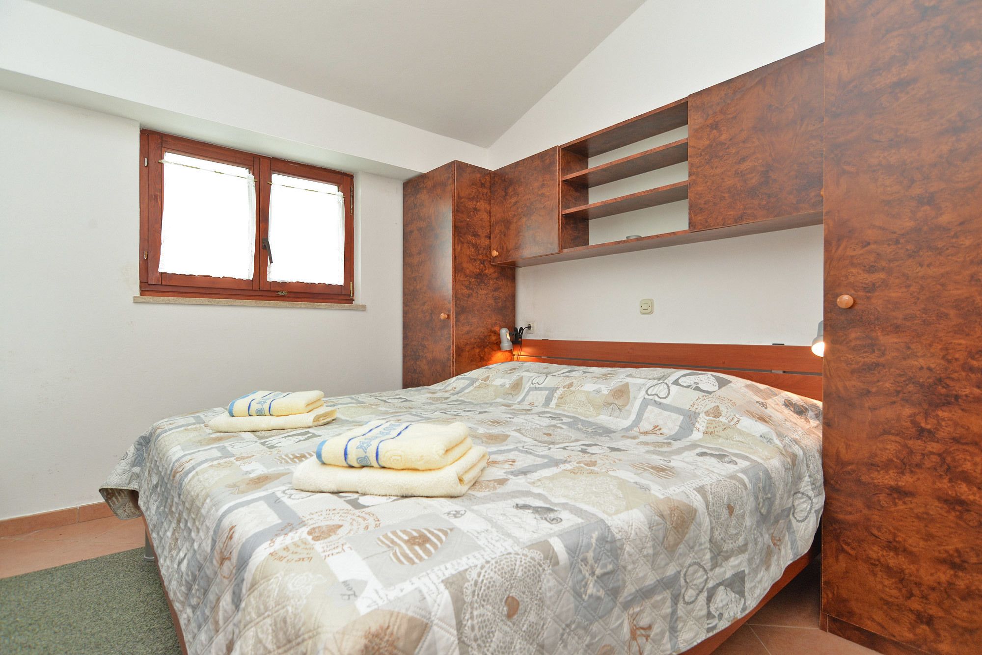 A bedroom with a bed, a window, and built-in wooden shelves.
