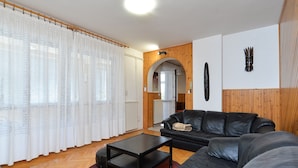 A modern living room with a black leather sofa, a black coffee table, and a red rug. There is a wooden wall panel and a white door with an archway leading to another room. - Apartment 531 (Pula)