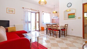 A living room with a red sofa, a glass coffee table, and a TV. There is a dining area with a table and chairs. The kitchen is visible in the background. - Apartment 539 (Medulin)