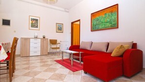 A living room with a red sofa, a dining table with chairs, a kitchen area, and a painting on the wall. - Apartment 539 (Medulin)